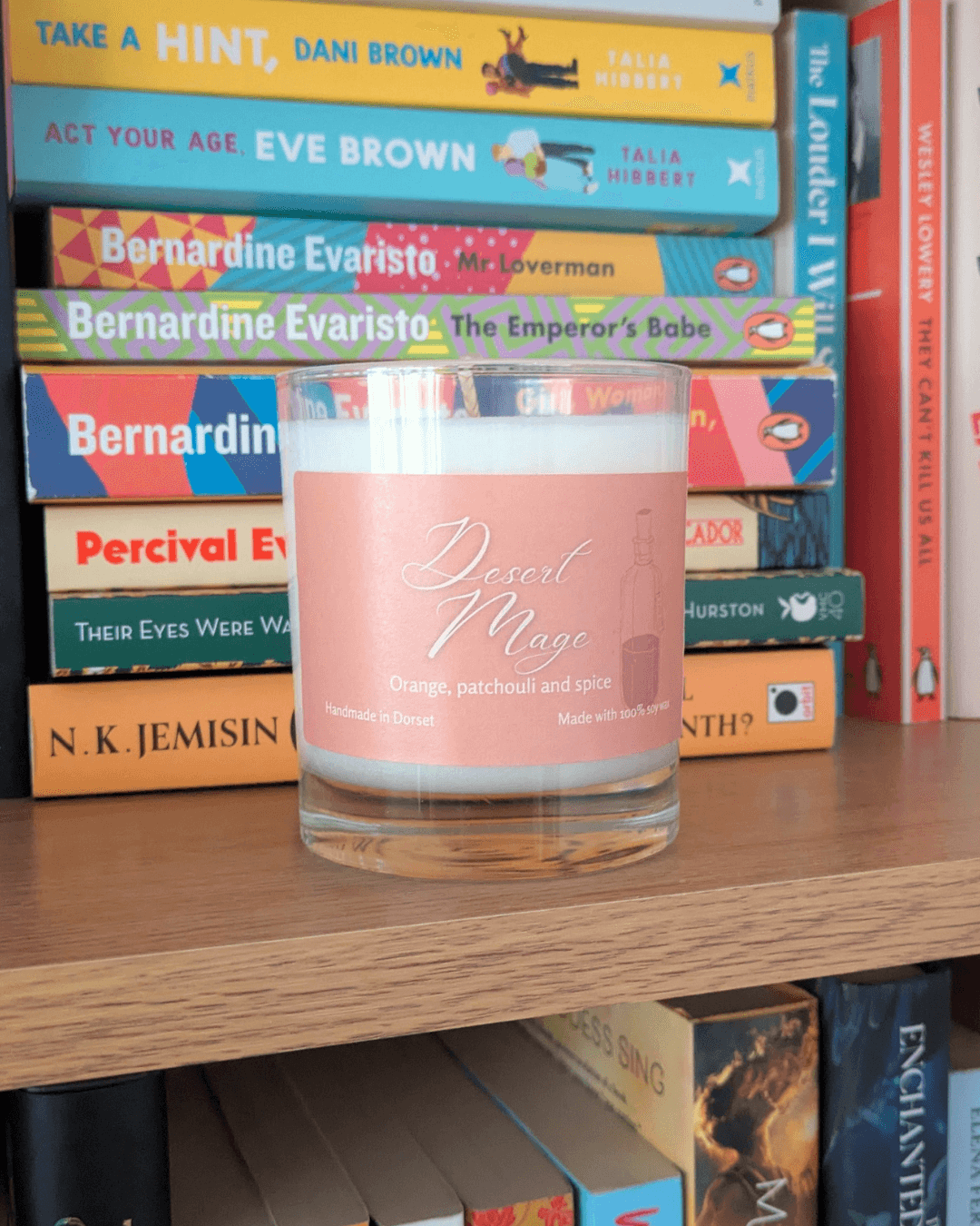 a soy candle with a pale orange label, reading 'Desert Mage'. The candle sits on a bookshelf in front of various books.