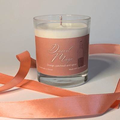 a soy candle with a pale orange label, reading 'Desert Mage'. the table in front of the candle is decorated with a ribbon in the same orange shade.