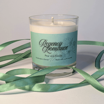 a soy candle with a mint-green label, reading 'Regency Romance'. the table in front of the candle is decorated with a ribbon in the same mint shade.