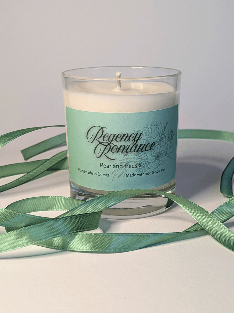 a soy candle with a mint-green label, reading 'Regency Romance'. the table in front of the candle is decorated with a ribbon in the same mint shade.